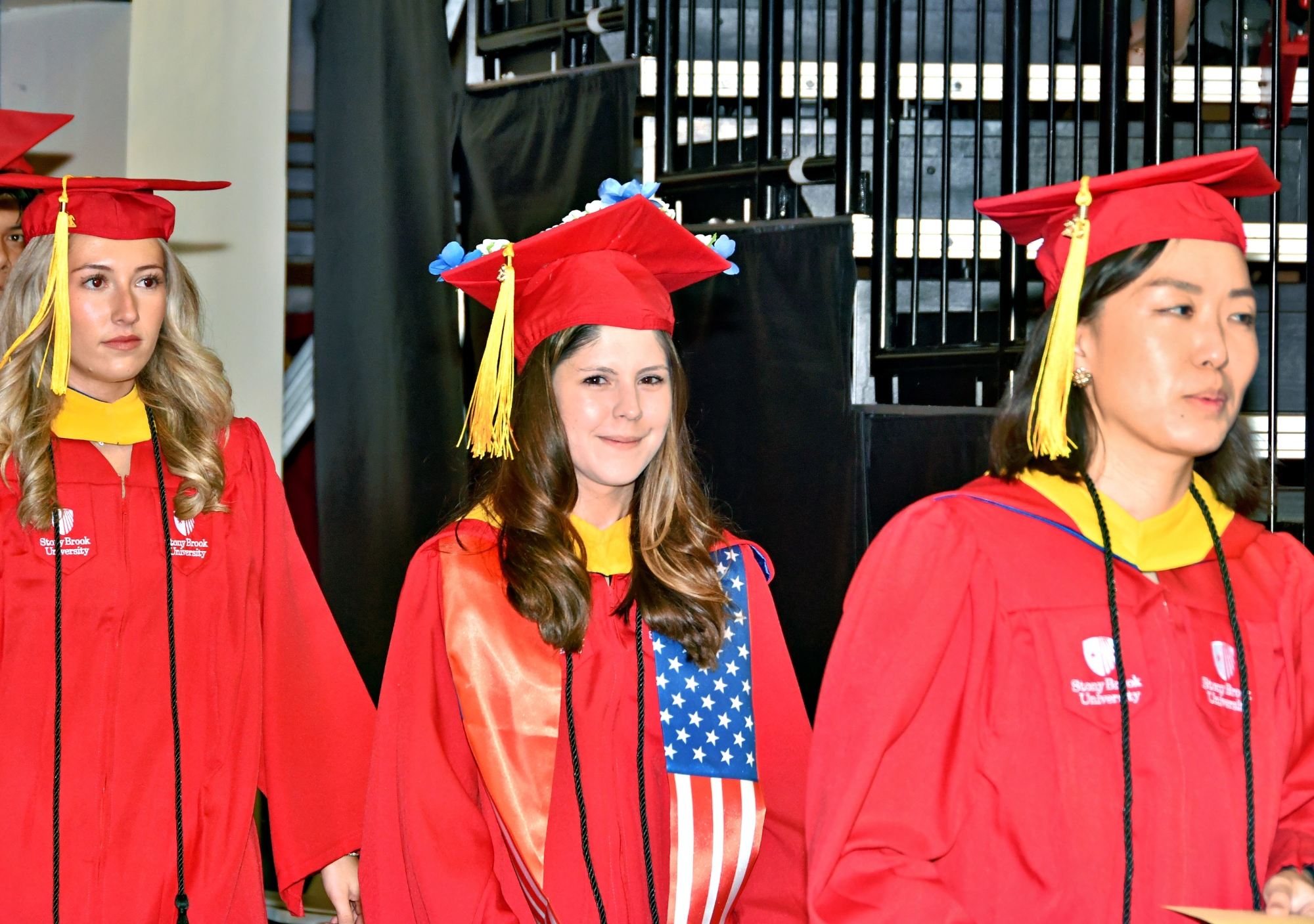 Stony Brook University College of Business Graduates in red caps and gowns standing together and smiling