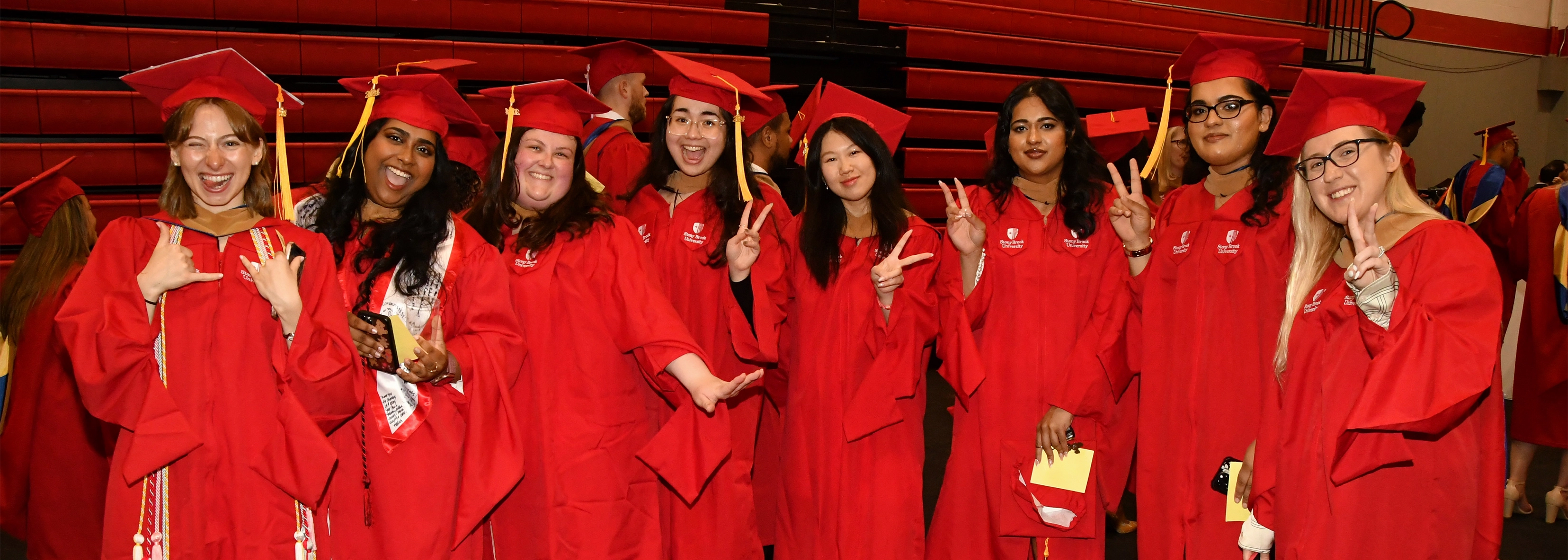 A group of Stony Brook University College of Business graduates wearing red caps and gowns standing together and smiling.
